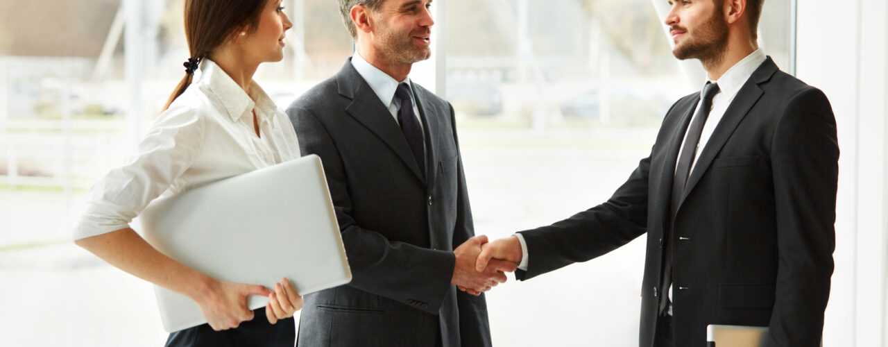 deux hommes se serrant la main avec une secrétaire à côté d'eux
